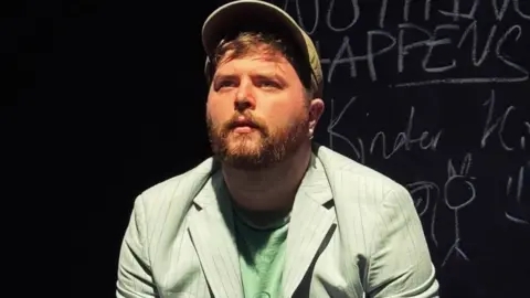 Actor on stage in a green jacket.