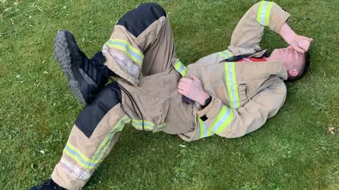 Chris Dabell Chris Dabell on the floor after a training run. He looks exhausted and is wearing full firefighters uniform.