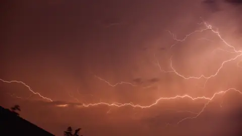 Mr Twister Red-coloured lightning striking sideways across the sky during night. 