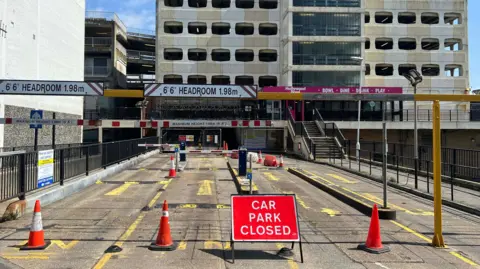 An image of the currently-closed Grafton multi-storey car park in Worthing. A closure sign can be seen alongside cones dotted across the entrance. 