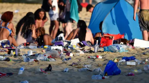 Image of rubbish on Bournemouth beach next to visitors who are enjoying the heatwave