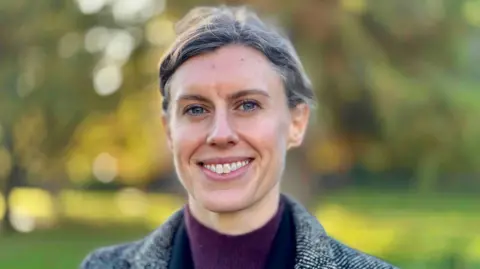 Getty Images Jessica Toale, a woman with short grey hair, is pictured smiling at the camera in a posed photograph. She is outside, with out-of-focus grass and trees in the background behind her. 
