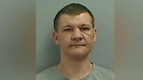 Cleveland Police Mugshot of a man with short dark hair and a scar across his nose and beneath his eye.