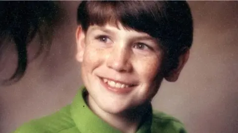 Family Handout Headshot of a young boy wearing a green shirt and smiling while look off camera.