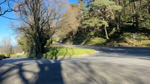 BBC The Ramsey Hairpin, a road with a sharp steep turn, there are trees on either side of the road.