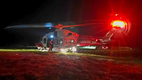 A slightly blurry picture of a helicopter with a bright red light on its tail blades