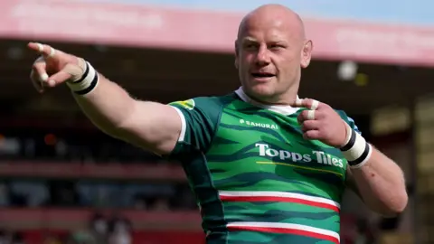 PA Media Dan Cole wears a green Leicester Tigers jersey, looking and pointing to the left of the frame. Behind him is a sporting stand.