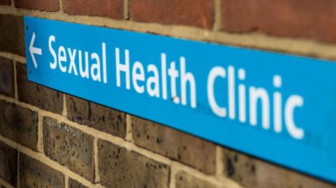 A blue sign for a sexual health clinic on a brick wall