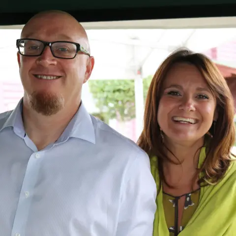 Family Photo A family photo showing a bald man with glasses and wearing a white shirt, alongside a woman with long auburn hair and a green top.