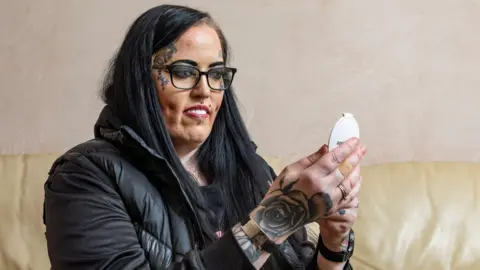 SWNS Stacey wearing her veneers and holding up a mirror