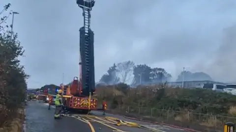 Nick Sumption A fire engine is parked on a road next to a field with smoke coming from it.