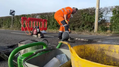 BBC Man in orange overalls fixing a pothole in Denby, Derbyshire 