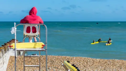 Rear view of a lifeguard sitting on a watchtower at the beach with surfers in the distance.