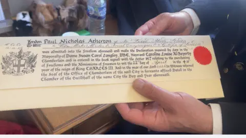 A long folded certificate written on sheepskin parchment paper, with a real wax seal on the right and a coat of arms on the left