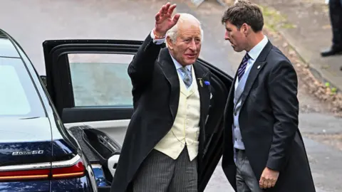 Reuters King Charles is waving to people after exiting a car through its door