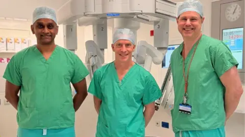 Sheffield Teaching Hospitals NHS Foundation Trust Three medical staff at Northern General Hospital, in Sheffield, including in the consultant surgeons Clive Kelty (in the centre of the image) and Martin Trotter (on the right) with an unnamed colleague on the left. All are wearing green hospital scrubs