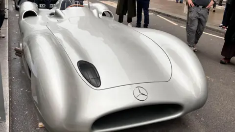 Asad Ahmad/BBC A silver Mercedes W196, a curved, futuristic-looking race car, parked on Pall Mall