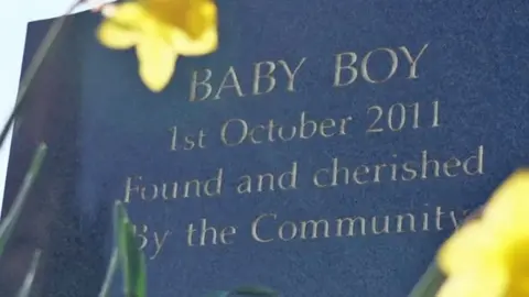 Black gravestone reading: Baby Boy 1st October 2011 Found and cherished by the community