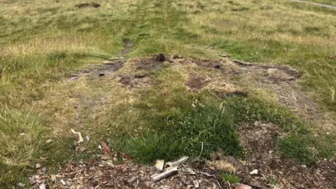 Grass has been worn away on the top of the mound where vehicles have driven