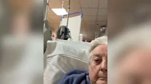 A woman lying on a hospital bed in a hospital corridor with temporary screens in the background