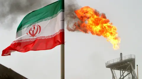 A gas flare on an oil production platform is seen alongside an Iranian flag.