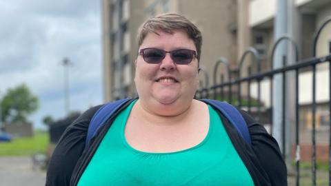 Woman stands outside high rise flats wearing green top