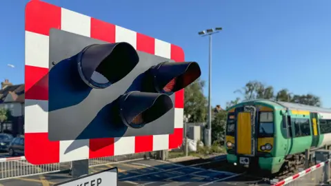 A railway level crossing with a green Southern train going across it.