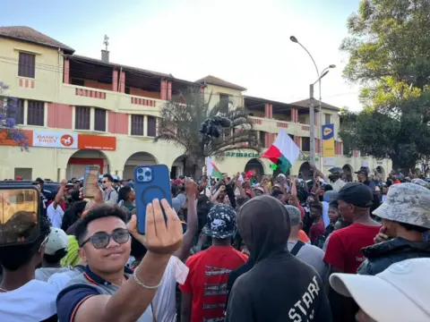 Protesters, including one taking a selfie, are outside the main square in Antananarivo on Sunday