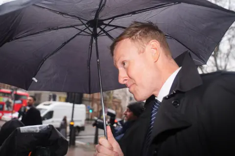 PA Media Richard Wells wearing a suit and holding an umbrella
