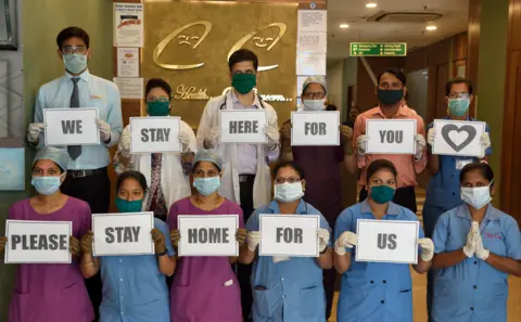 Getty Images Indian hospital workers hold signs that say: 'we stay here for you please stay home for us'
