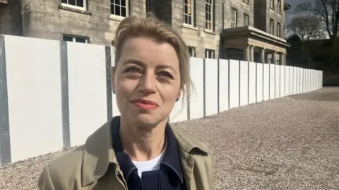 Photograph of Kate Brindley, the Head of Cultural Programming at Haigh Hall. She is pictured in front of the building, which has been wooden boards surrounding it.
