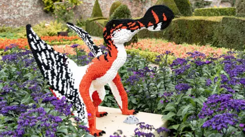 East Riding of Yorkshire Council A Lego model dinosaur, made from red, black and white bricks, sits in a bed of purple flowers at Sewerby Hall