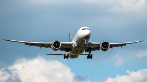 Getty Images An aeroplane, viewed from the ground, is flying through a blue sky