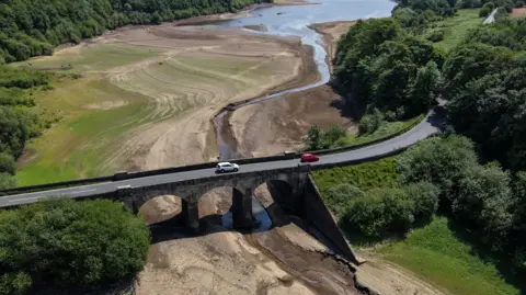 Reuters A drone view shows vehicles passing over a bridge across a dry section of the Lindley Wood Reservoir, which has been largely drained.
