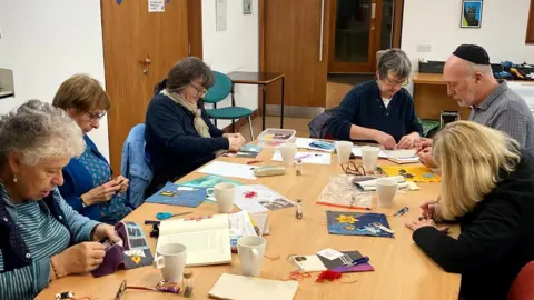 Six people around the table creating the squares for the quilt