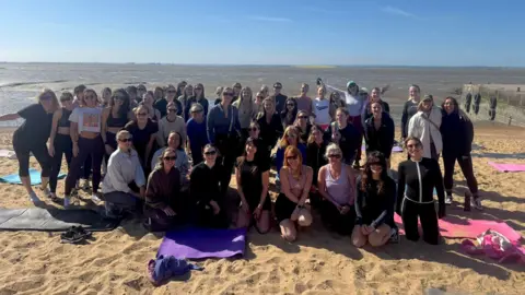 Alexandra Beard A group of people posing for a picture on a beach with yoga mats lying around