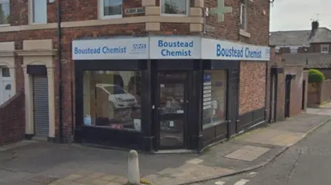 Boustead Chemist, which is located on the corner of the street. It has large windows and black wooden panelling. It stands at the end of row of terraced houses.