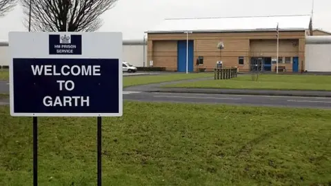 External view of HMP Garth with a close up of a sign saying 'Welcome to Garth' with the prison building in the background.