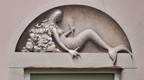 Paul Czainski A stone door with a mermaid appearing to be carved into the frame