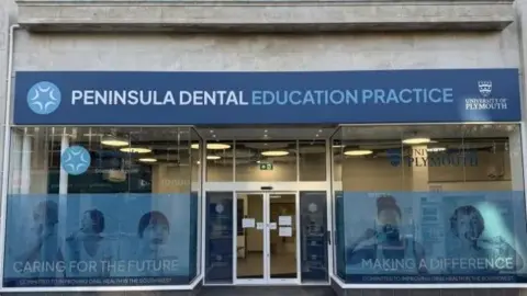 Peninsula Dental Social Enterprise The exterior of a shop with blue branding and a sign for the Peninsula Dental Education Practice