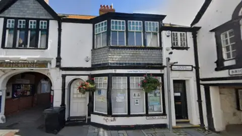 Google Street View of Guildhall Cottage - an old, terraced, two-storey, black and white building with bay windows on both the ground and first floor.