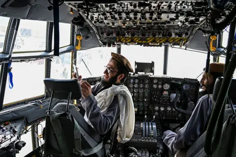 Wakil Kohsar / AFP Taliban fighters sit in the cockpit of an Afghan Air Force aircraft at Kabul airport on 31 August 2021