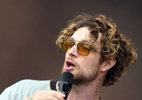 PA Media Tom Grennan wearing tinted sunglasses as he sings into a microphone