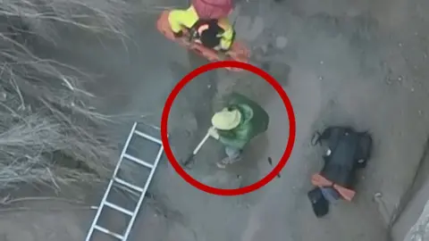 Ladders works to rescue a hiker stuck in quicksand (circled).