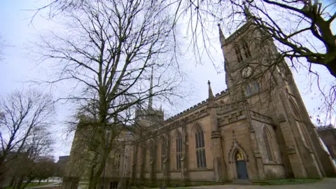 Exterior view of Blackburn Cathedral surrounded by trees in the grounds of the sandstone building