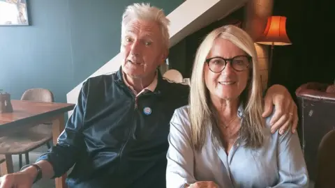 Georgie Marshall Georgie Marshall and her husband Barrie sat on a sofa smiling at the camera