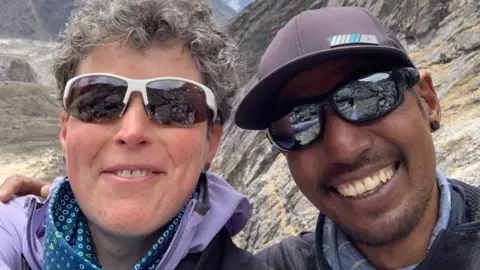 Shaunna Burke Shaunna Burke in Nepal with a Sherpa friend who is wearing sunglasses and a cap.