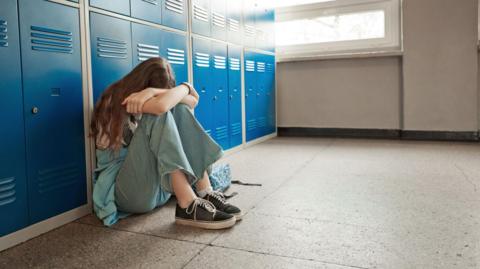 Teenager sits on floor near lockers