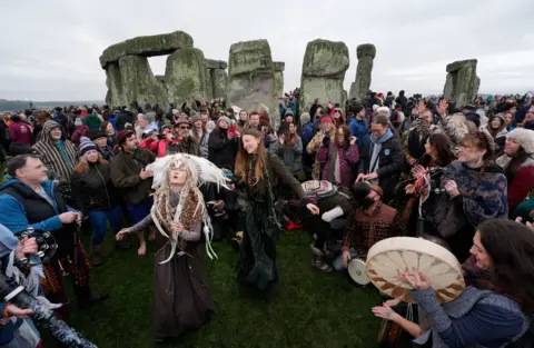 PA Media Kefan Wang (left), 4th-generation Manchu Shaman, dances as people take part in the winter solstice celebrations during sunrise at the Stonehenge