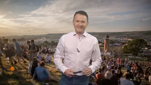 Matt Taylor standing in front of a picture of a field at Glastonbury